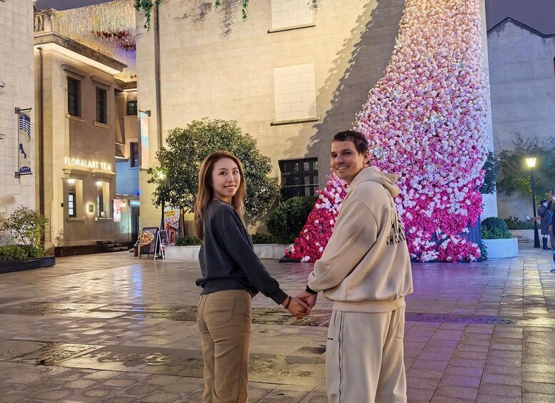 A couple holding hands in front of a building with a large floral display. 5
