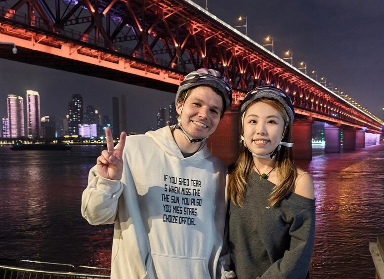 Two people standing in front of a lit bridge with a city skyline in the background. 2