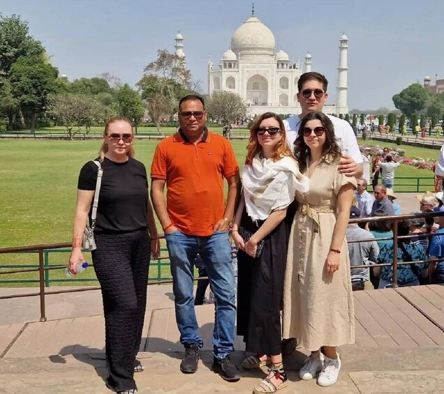 A group of people standing in front of the Taj Mahal with a park and visitors in the background. 2