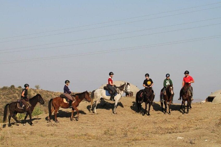 Een groep mensen rijdt paard over een droog, grasveld onder een heldere lucht. 4