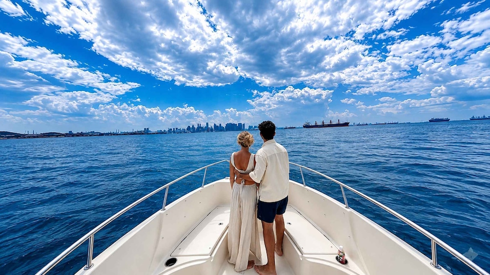 A couple on a boat with a city skyline and cargo ships in the background. 3