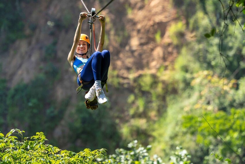 A person suspended in mid-air by a zip line, surrounded by lush greenery and a rocky cliff. 3