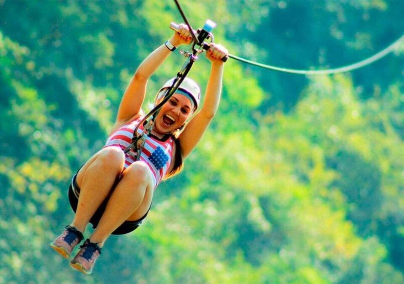 A person bungee jumping with a harness and safety gear, suspended in mid-air against a backdrop of lush green trees. 1