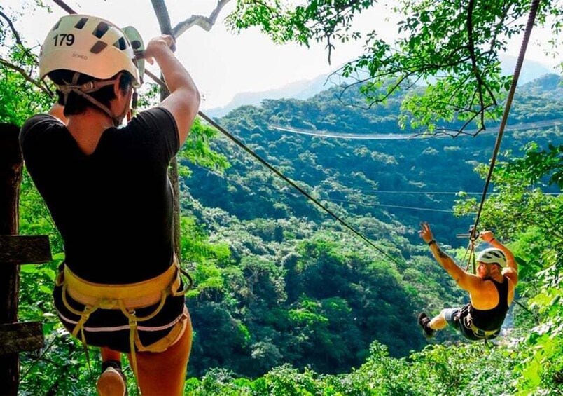 Two people zip-lining through a lush forest with a winding road in the background. 2