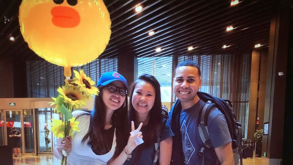 Three people posing with a large yellow balloon and sunflowers in a modern indoor setting. 5