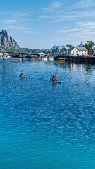 Two paddleboarders on a calm river with a mountain in the background and buildings along the shore. 1