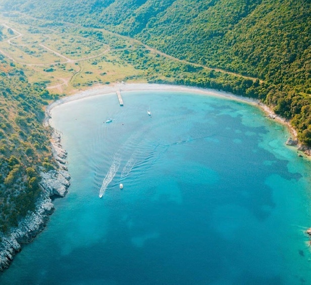 An aerial view of a coastal area with clear turquoise waters, a sandy beach, and lush green hills. 1