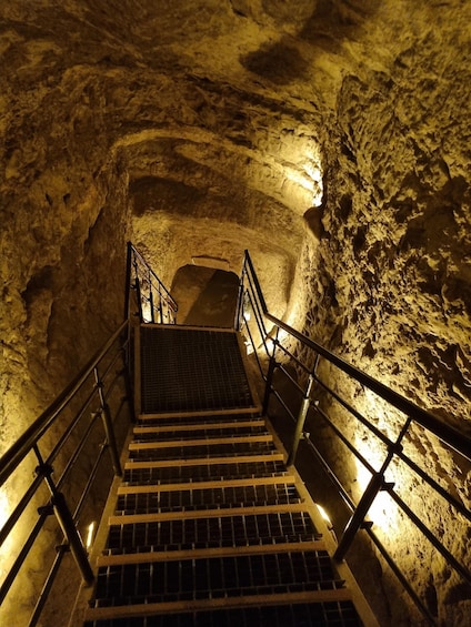 A staircase in a cave with metal railings and a metal grate at the bottom. 4