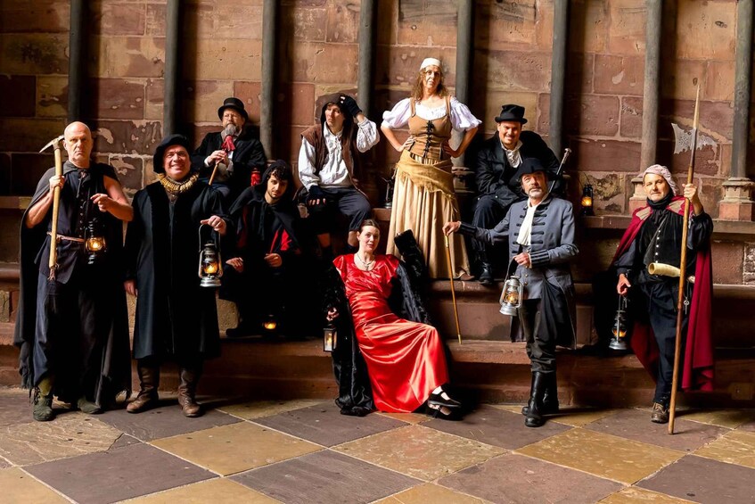 A group of people in historical costumes standing in an indoor setting with stone walls and a tiled floor. 3