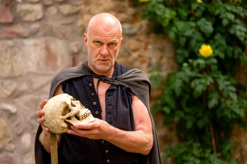 A person holding a skull outdoors with a stone wall and greenery in the background. 5