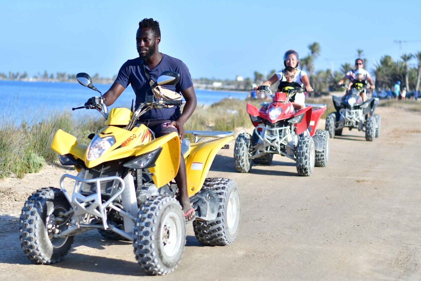 A person riding a yellow ATV on a dirt road with a body of water in the background. 2