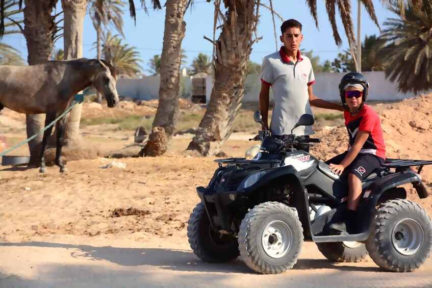 A person riding an ATV on a sandy terrain with palm trees in the background. 3
