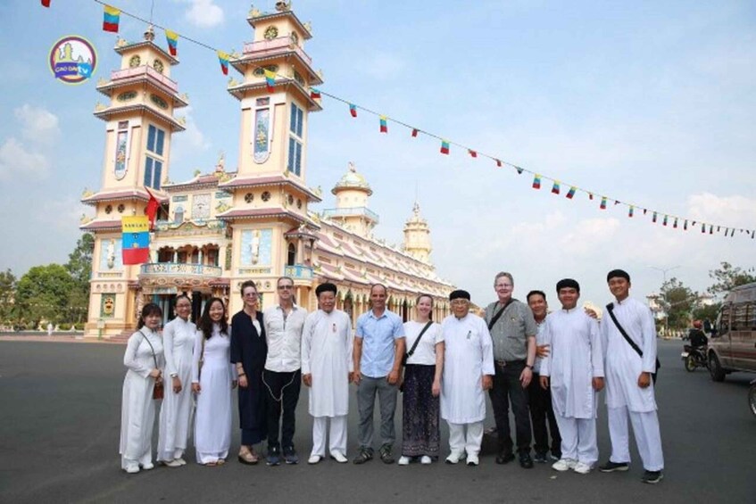 A group of people standing in front of a large, ornate building with multiple towers and flags. 3
