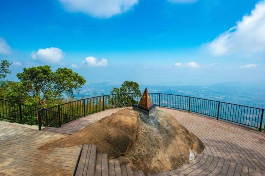 A viewpoint with a wooden platform, a metal railing, and a rocky hill with a monument. 2