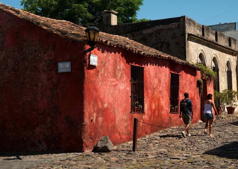 A red building with a sign, a cobblestone street, and a person walking. 3