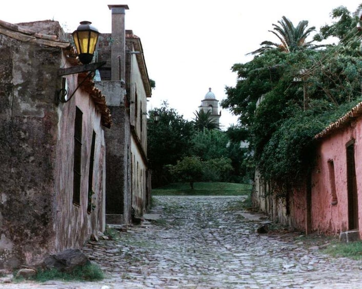 A cobblestone street flanked by old buildings with a lamp post and a dome structure in the distance. 4