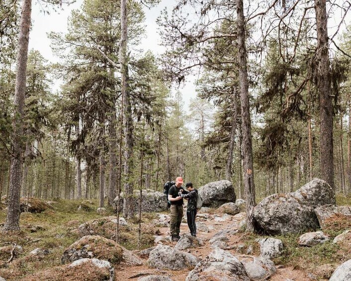 Two people hiking in a forest with large rocks on the trail. 1