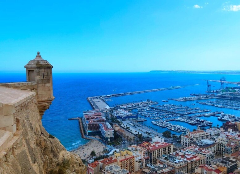 A coastal city with a historic tower, a marina, and a rocky cliff. 3