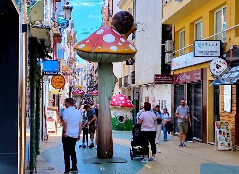 A street with people walking, shops, and a large mushroom sculpture. 5
