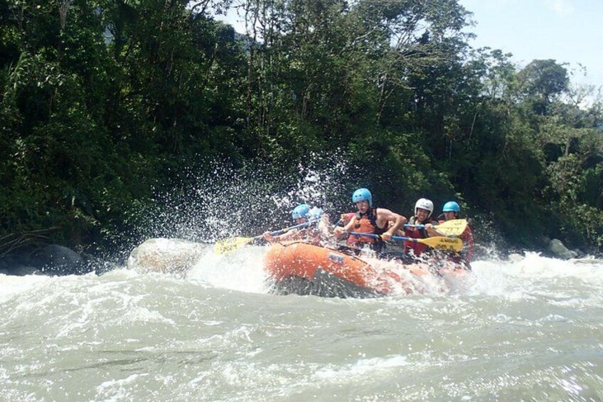 A group of people in an orange raft navigating through a river surrounded by dense greenery. 1