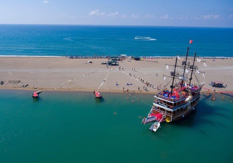 A large cruise ship docked at a beach with people walking and swimming in the water. 3
