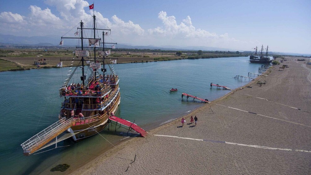 A large ship docked at a beach with people on board and a smaller boat nearby. 4