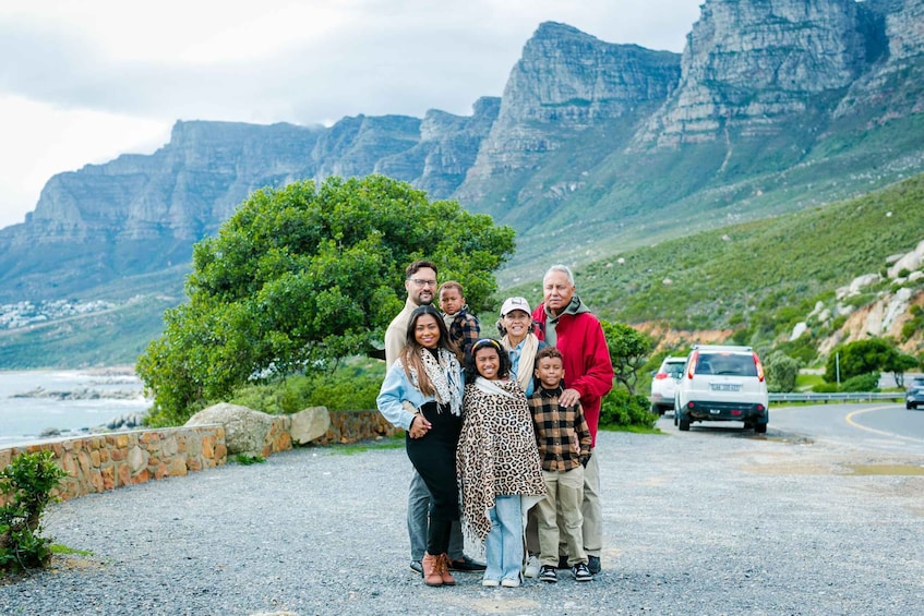 A family of seven posing on a gravel road with a mountainous backdrop and a body of water. 3