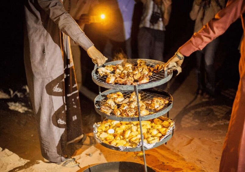 A person grilling chicken on a three-tiered grill outdoors at night. 2