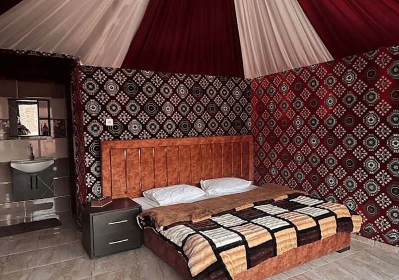 A bedroom with a patterned wall, a wooden headboard, a bed with a quilt, a bedside table, and a mirror. 3