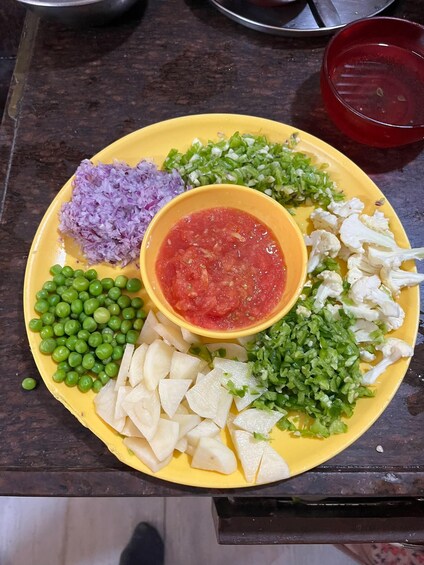 A yellow plate with various chopped vegetables and a bowl of red sauce. 4