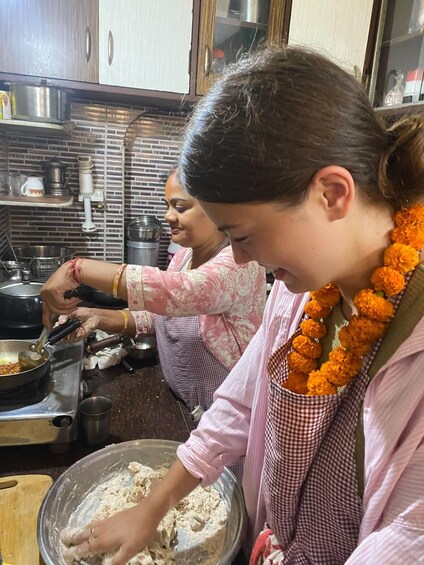 A kitchen with two individuals cooking, one stirring a pan and the other mixing dough. 2