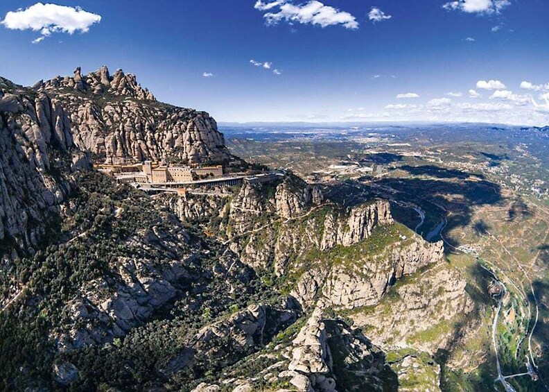 A mountainous landscape with a large rock formation and a building perched on top. 4