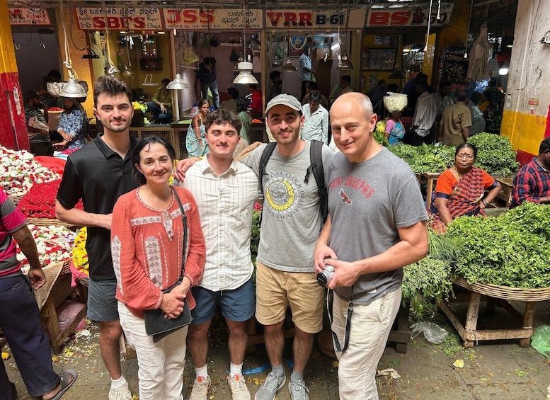 A group of people standing in a market with various stalls selling flowers and vegetables. 5