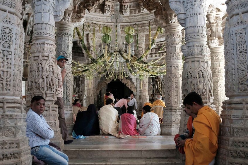 A group of people in traditional attire at a temple with intricate carvings and a hanging chandelier. 5