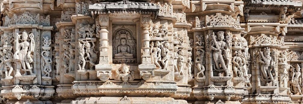 A detailed stone carving of a deity surrounded by attendants, set within a temple's ornate architecture. 2