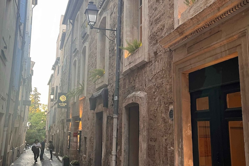 A narrow urban street with historic buildings, a lamp post, and a few pedestrians. 3