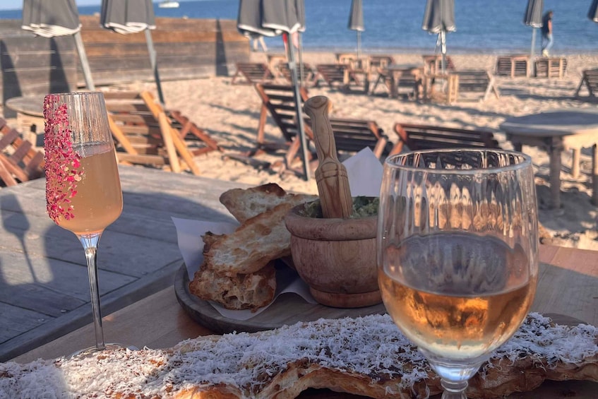A beachside table with a cocktail, a glass of white wine, and bread. 5