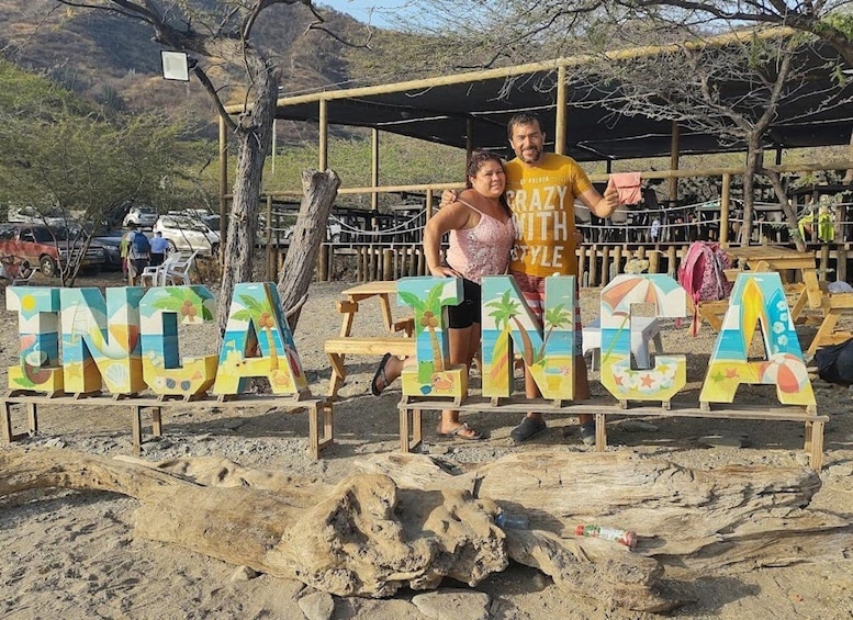 A beach with wooden letters spelling 'INCA INCA' and a couple standing in front. 5