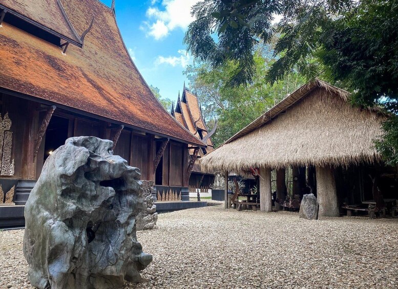 A traditional wooden building with a thatched roof, surrounded by trees and a large rock formation. 1