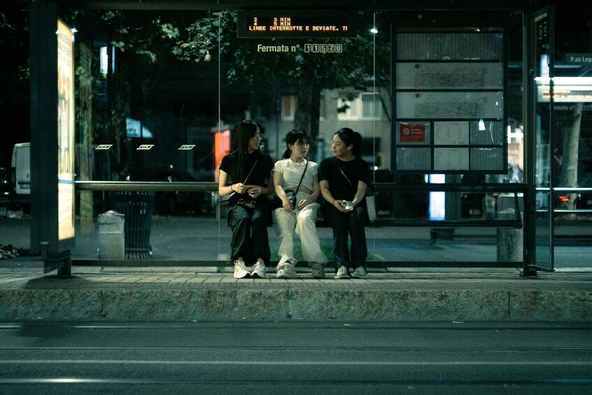 Three people sitting on a bus stop bench at night. 2