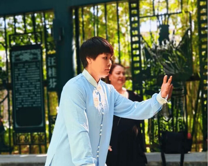 A person in a light blue traditional outfit standing in front of a green gate with a signboard. 2