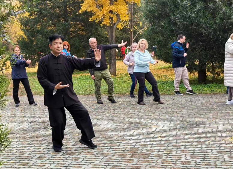 A group of people practicing martial arts outdoors on a paved path surrounded by trees. 5