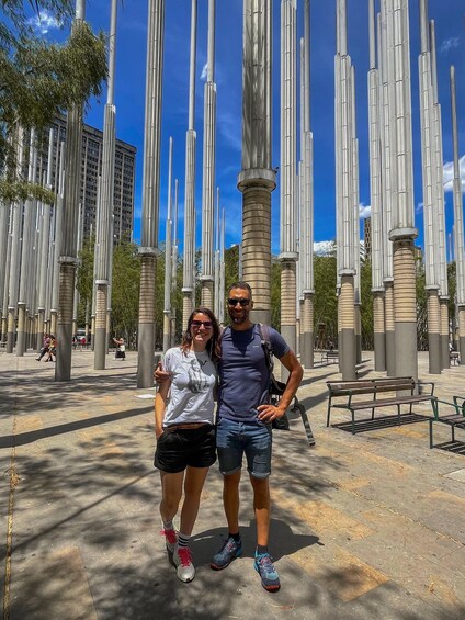 A couple standing in a plaza with tall, slender columns and benches. 1