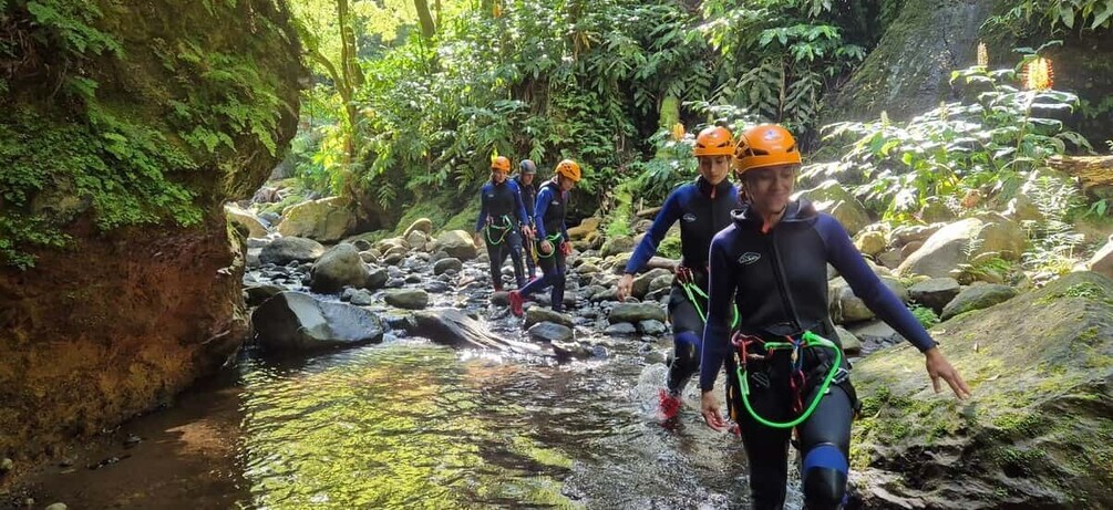 People in wetsuits and helmets crossing a rocky stream in a forested area. 5