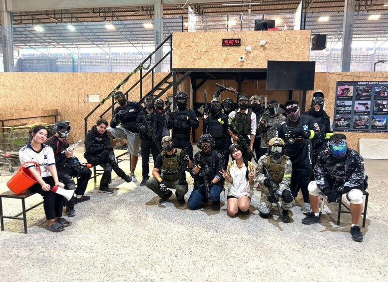 A group of people in tactical gear posing for a photo in an indoor setting with a wooden structure and a digital clock displaying 15:00. 5