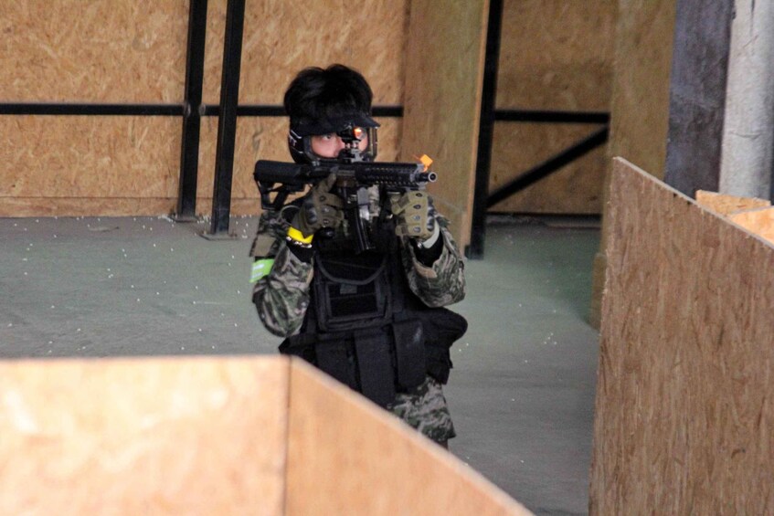 A person in military attire aiming a rifle in an indoor shooting range. 4