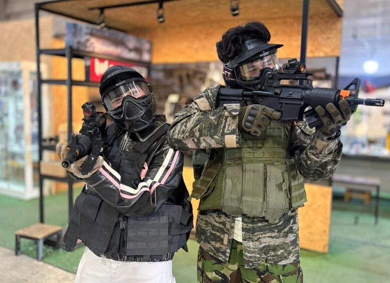 Two individuals in tactical gear, one holding a rifle, in an indoor shooting range. 1