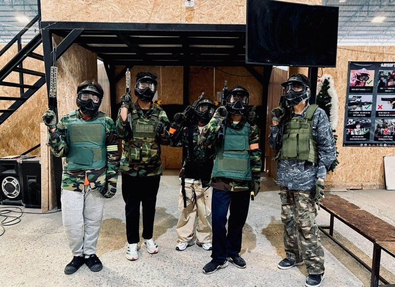 Five people in tactical gear standing in front of a wooden structure. 3