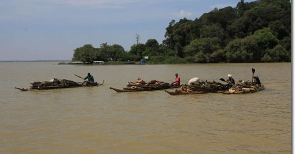 Three longboats on a river with people paddling them. 4