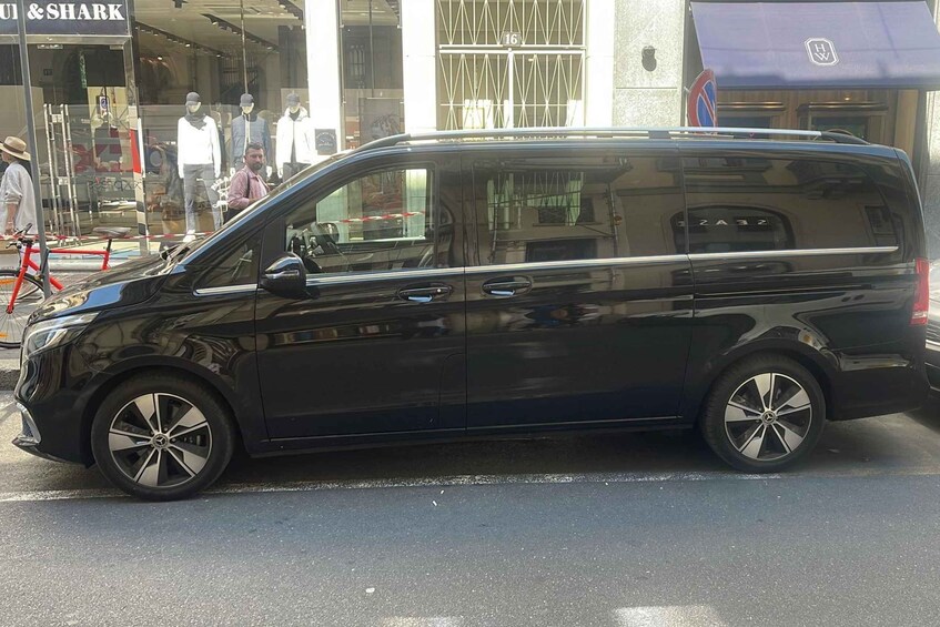 A black van parked on a street with a storefront in the background. 2